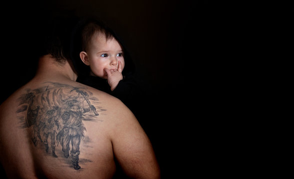 Tattooed Father from Behind Holding baby on the black background. Baby with horn hand - Hard Rock symbol. copy space