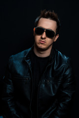 Fototapeta premium Young sexy stylish guy with glasses in a black leather jacket on a black background