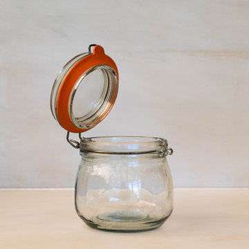 An empty Kilmer round clip top glass storage jar with an orange rubber seal.  The jar lid is open and the objects is isolated against a plain white background 