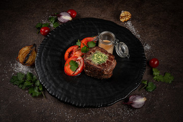 Meat medallion with mushrooms on a round white plate on a dark brown background. restaurant menu
