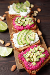 Variation of healthy sandwiches with avocado beetroot cream cheese and whole wheat rye bread on wooden background. Delicious snacks and toast. Food composition, tasty italian meal. Close up
