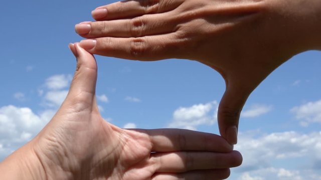 Closeup point of view video footage of two female hands making frame gesture using her both hands and looking through hole at beautiful sunny summer blue sky with soft fluffy clouds. 