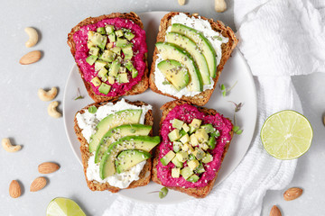 Variation of healthy sandwiches with avocado beetroot cream cheese and whole wheat rye bread on a plate on grey background. Delicious snacks and toast. Food composition. Top view
