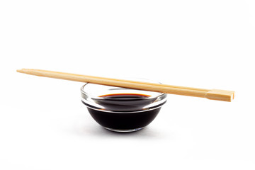 Soy sauce in a glass gravy boat with Chinese chopsticks on a white plate, isolate