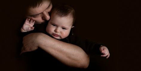 Dad hugging and kissing his baby on the black background. Love and care of father for baby concept.