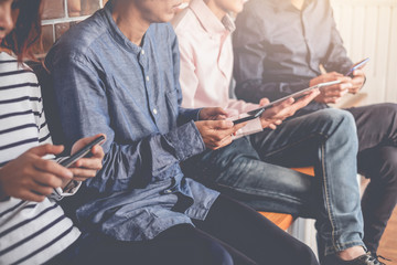 Group of young people in casual clothes sitting using digital tablet and smartphone.