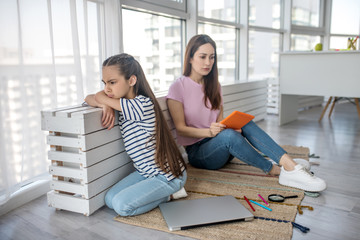 Sad mom and daughter sitting on rug on the floor.