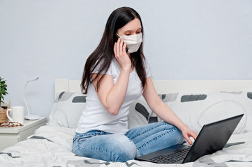 Work Home or Distance Online Learning on Quarantune. Woman in Protective Face Mask Remotely Working on Bed Using Laptop and Talking on Phone