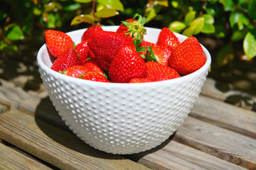 Strawberry berries in a white bowl on a wooden background.