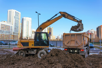 Excavator pours soil into the back of a truck during repair of heating main on road in residential multi storey area of city