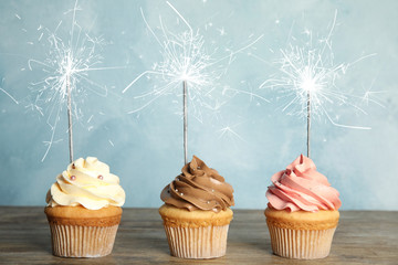 Birthday cupcakes with sparklers on wooden table against light blue background