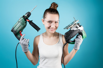 A cunningly smiling girl and power tools in her hands - a jigsaw and a drill