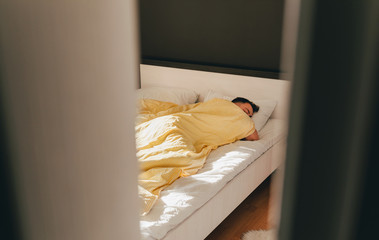 A sleeping man in a bed with yellow striped blanket in sunny bedroom. Good morning mood