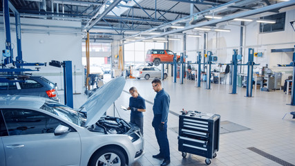 Two Mechanics in a Service are Inspecting a Car After They Got the Diagnostics Results. Female...