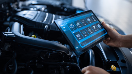 Fototapeta Car Service Manager or Mechanic Uses a Tablet Computer with a Futuristic Interactive Diagnostics Software. Specialist Inspecting the Vehicle in Order to Find Broken Components In the Engine Bay. obraz
