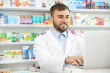 Naklejka na ściany i meble Professional pharmacist working on laptop in modern drugstore