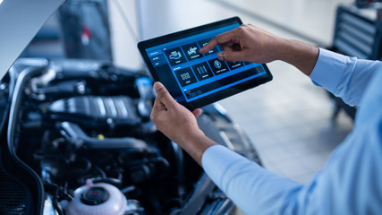 Car Service Manager or Mechanic Uses a Tablet Computer with a Futuristic Interactive Diagnostics Software. Specialist Inspecting the Vehicle in Order to Find Broken Components In the Engine Bay.