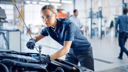 Beautiful Empowering Female Mechanic is Working on a Car in a Car Service. Woman in Safety Glasses is Fixing the Engine. She's Using a Ratchet. Modern Clean Workshop with Cars. 