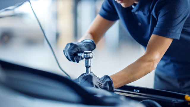 Close Up Shot of a Female Mechanic Working on a Car in a Car Service. Empowering Woman Makes an Usual Car Maintenance. She's Using a Ratchet. Modern Clean Workshop. 