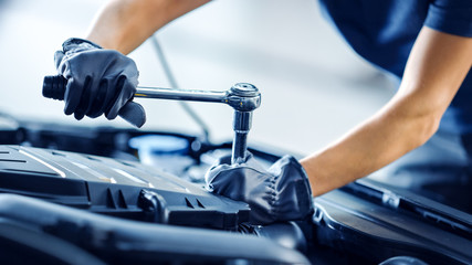 Close Up Shot of a Professional Mechanic Working on Vehicle in Car Service. Engine Specialist Fixing Motor. Repairman is Wearing Gloves and Using a Ratchet. Modern Clean Workshop.  - obrazy, fototapety, plakaty