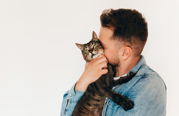 A young man in blue denim shirt is holding and hugging a cute funny brown tabby cat. Home pets....