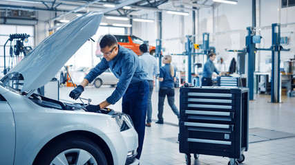 Professional Mechanic is Working on a Car in a Car Service. Repairman in Safety Glasses is Working...