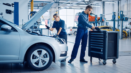 Two Mechanics in a Service are Inspecting a Car After They Got the Diagnostics Results. Female...