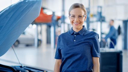 Beautiful Empowering Female Car Mechanic is in a Vehicle Service. She Looks Happy, Smiles and Looks...