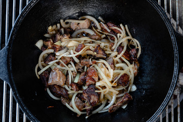 Pieces of lamb with onion are fried in boiling oil on the fire. As a stage in the preparation of traditional pilaf.step-by-step process of cooking pilaf in a cast iron cauldron on grill.