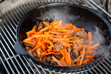 Pieces of lamb with onion are fried in boiling oil on the fire. As a stage in the preparation of traditional pilaf.step-by-step process of cooking pilaf in a cast iron cauldron on grill.