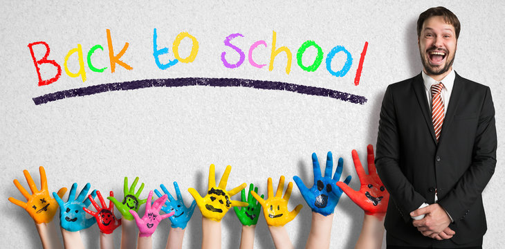 message BACK TO SCHOOL on a wall with many painted kids hands and a male teacher