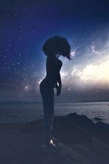 Woman's silhouette standing on a beach with the milky way on the background