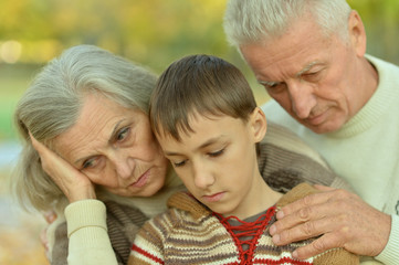 Sad grandfather, grandmother and grandson hugging in park