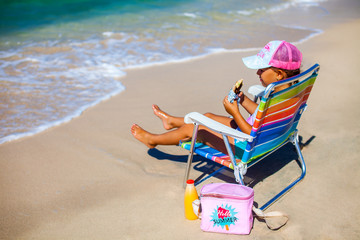 Little girl is on vacation sitting near the sea on beachchair with juice and snacks