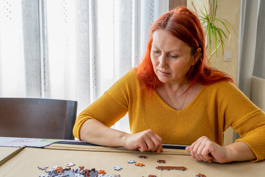 Beautiful redhead woman in a yellow sweater doing a puzzle in the living room at home