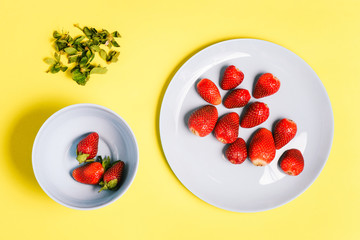 Two blue plates with strawberries on a yellow background. Scrubbing strawberries from green leaves.