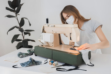 Girl sewing protective medicine mask on sewing machine at home to prevent the flu. Covid-19 in the room with white background