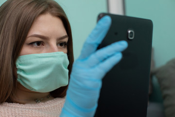 A high school graduate sitting on a bed with a tablet in hand in rubber gloves and a protective...