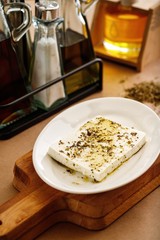 Authentic greek feta cheese with herbs and olive oil in white plate. Presentable plating of cheese on wooden table background. Food photography concept for restaurant book menu.