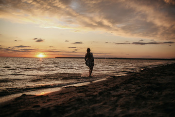 Fototapeta premium blonde girl walk along the beach by driving at sunset in a beautiful dress, beautiful evening on the river, beautiful sunset