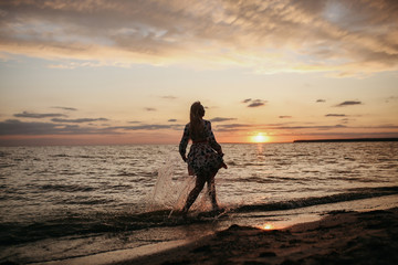 
blonde girl walk along the beach by driving at sunset in a beautiful dress, beautiful evening on the river, beautiful sunset