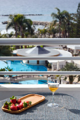 Obraz premium A glass of white wine stands on a table on the hotel balcony overlooking the pool and sea. Time relax.