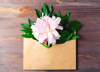 composition on a dark wooden background. open envelope from kraft paper with peonies in it. minimal holiday concept, top view