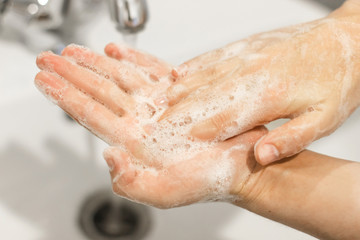 Washing hands. Rubbing palms, washing hands with antibacterial soap and in proper technique on background of flowing water in white bathroom. Prevention coronavirus. Cleaning and disinfecting hands