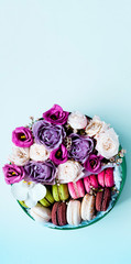 Festive concept from rosebuds in full bloom and Multicolored Macaroons on blue background. Mothers Day concept. Food decor. Close-up