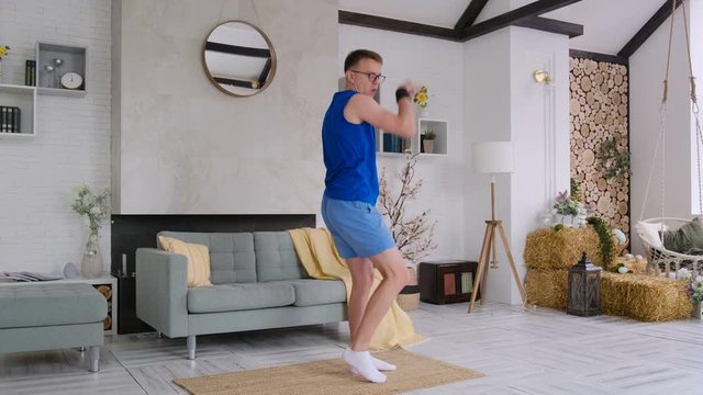 Cheerful energetic guy in sportswear and glasses dancing at home rejoicing at something