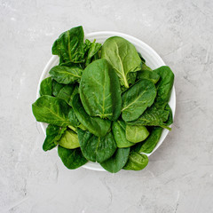 Clean food concept. Leaves of fresh organic spinach greens in a plate on a light background....