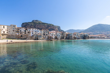 Fototapeta premium Idyllic view of turquoise sea and houses with Rocca di Cefalu rocky mountain in the background seen from historical old port of Cefalu, Sicily, Italy.