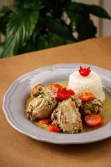 Greek chicken curry with coconut milk and sliced cherry tomatoes rice on the side on a plain white plate wooden table background. Authentic Mediterranean dish.