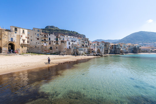 Idyllic view of turquoise sea and houses with Rocca di Cefalu rocky mountain in the background seen from historical old port of Cefalu, Sicily, Italy.